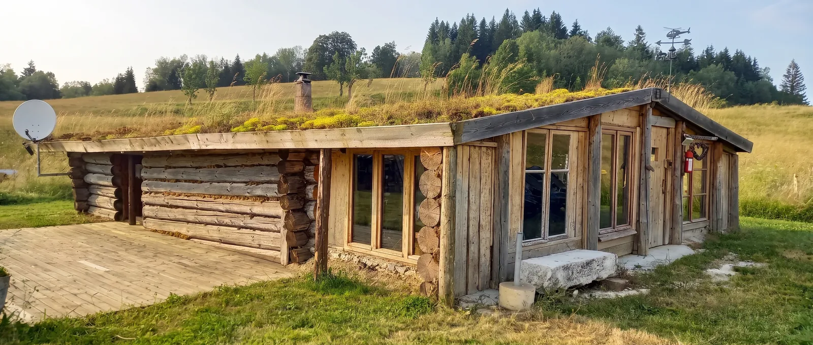 La Fuste en été : cabane en rondins au toit végétalisé, avec sa terrasse en bois