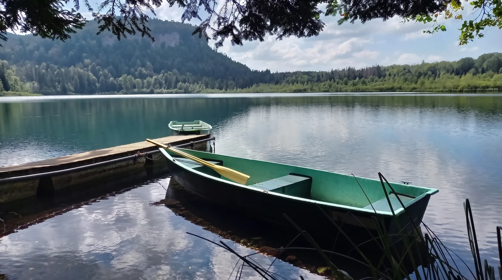 Une barque amarrée sur un lac, au pied d'une falaise boisée
